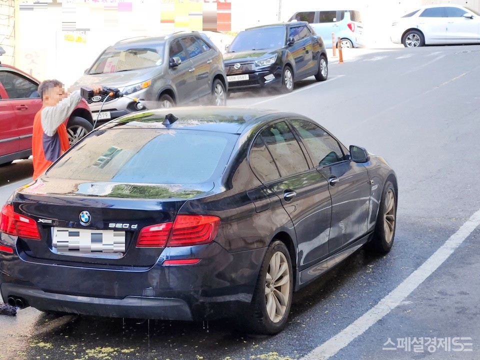 BMW의 중형 디젤 세단 운전자가 서울 주택가에서 세차하고 있다. 주택가 세차는 불법이다. [사진=정수남 기자]